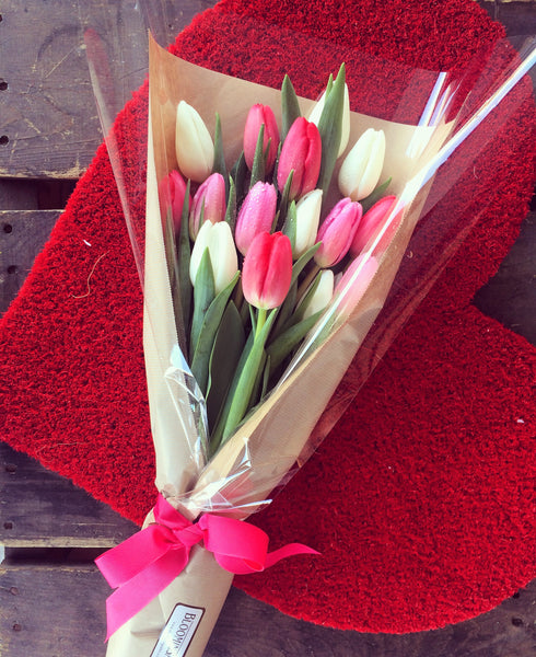 Bunch of tulips wrapped in brown paper with a pink ribbon.